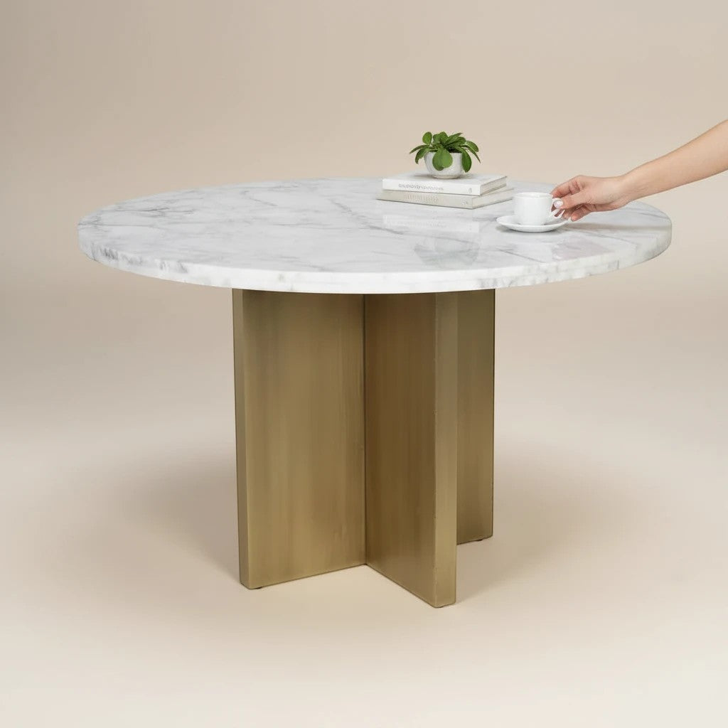 Trộm vía round white marble dining table with unique veining and a brushed gold pedestal base. Includes books and a plant.