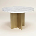 Trộm vía round white marble dining table with unique veining and a brushed gold pedestal base with a cross-leg design.